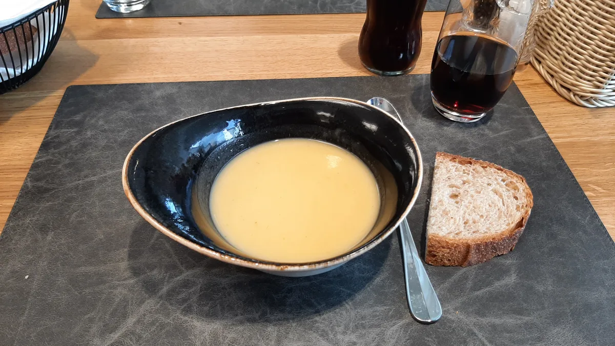 Eine Suppe in einem ovalen Teller, daneben ein Stück Brot.